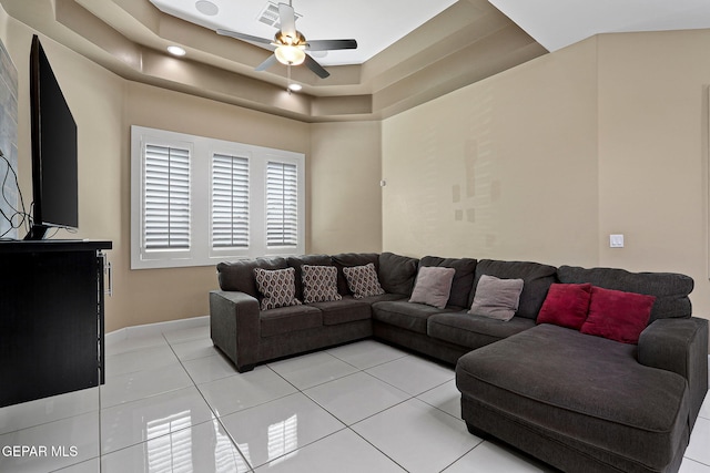 living room with a raised ceiling, light tile patterned floors, and ceiling fan