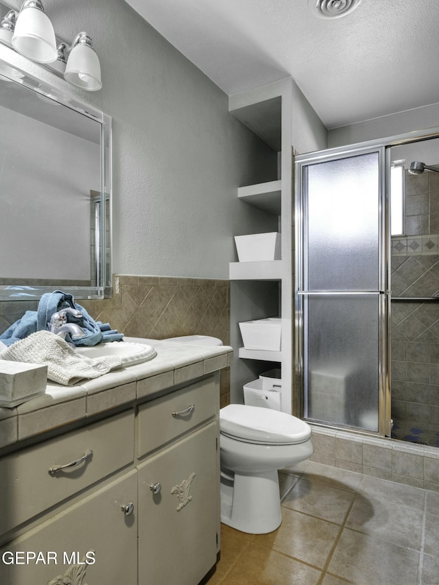 bathroom featuring tile patterned floors, toilet, a textured ceiling, vanity, and a shower with door