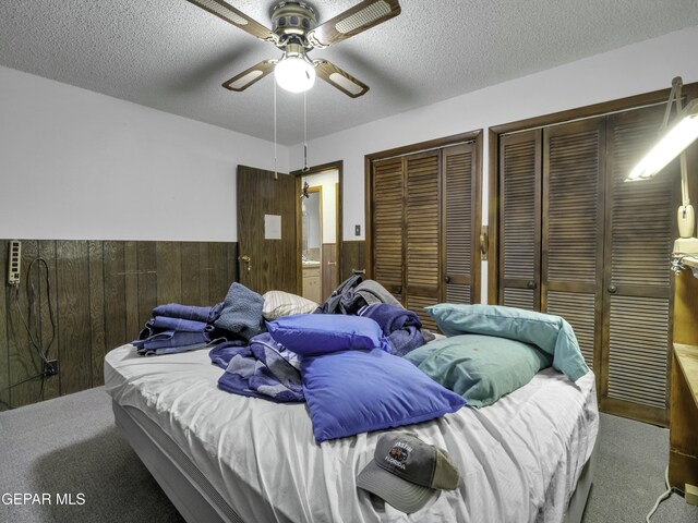 carpeted bedroom featuring ceiling fan, two closets, a textured ceiling, and wood walls