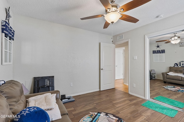 living area with ceiling fan, wood-type flooring, and a textured ceiling