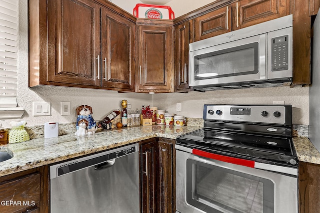 kitchen featuring light stone counters, dark brown cabinets, and stainless steel appliances