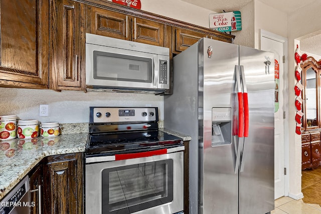 kitchen featuring light stone counters, dark brown cabinetry, stainless steel appliances, and light tile patterned flooring