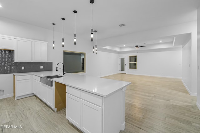 kitchen featuring white cabinetry, sink, decorative backsplash, hanging light fixtures, and a raised ceiling