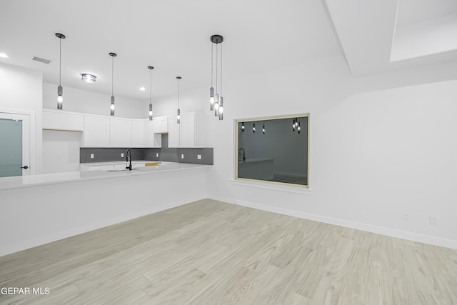 kitchen with sink, white cabinetry, decorative light fixtures, light hardwood / wood-style flooring, and backsplash