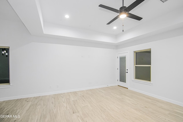 unfurnished room featuring a raised ceiling, ceiling fan, and light wood-type flooring