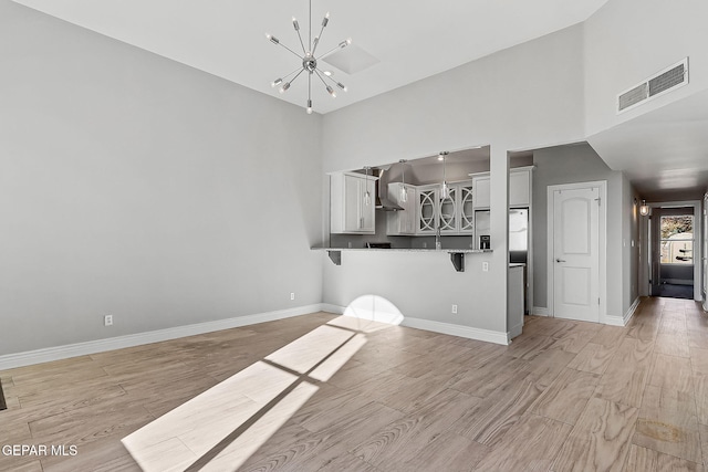 unfurnished living room with a notable chandelier, a towering ceiling, and light hardwood / wood-style flooring