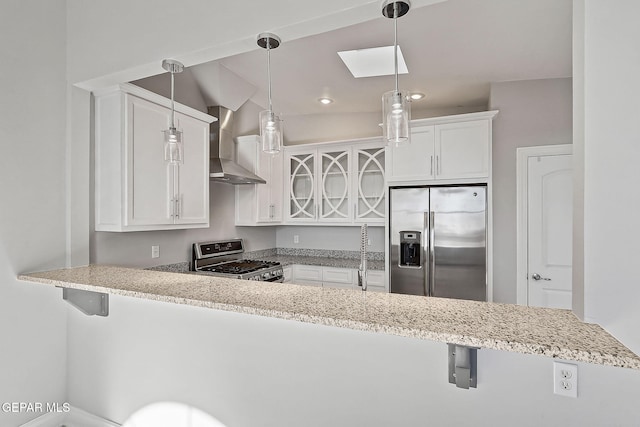 kitchen with appliances with stainless steel finishes, kitchen peninsula, white cabinets, pendant lighting, and wall chimney range hood