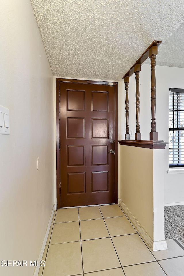 doorway to outside with a textured ceiling and light tile patterned floors