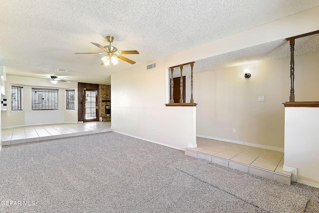 carpeted empty room with ceiling fan, a brick fireplace, and a textured ceiling