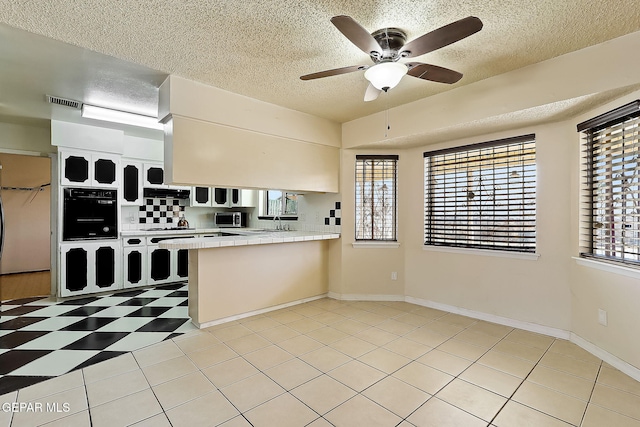 kitchen with ceiling fan, white cabinets, a textured ceiling, tile countertops, and oven