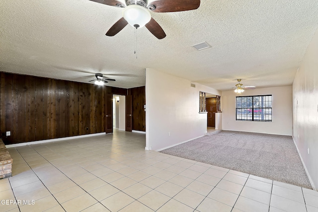 empty room with light carpet, a textured ceiling, and wood walls