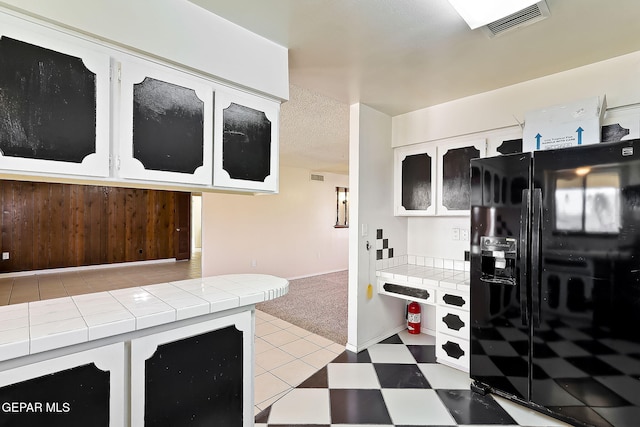 kitchen featuring white cabinetry, tile counters, light colored carpet, and black refrigerator with ice dispenser