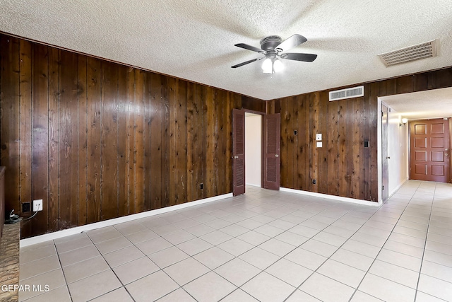 spare room featuring ceiling fan, wooden walls, light tile patterned floors, and a textured ceiling