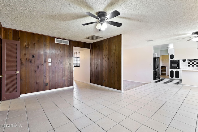 tiled empty room featuring a textured ceiling, wooden walls, and ceiling fan