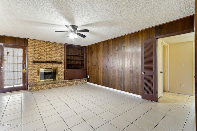 unfurnished living room featuring built in features, wooden walls, a fireplace, light tile patterned floors, and a textured ceiling