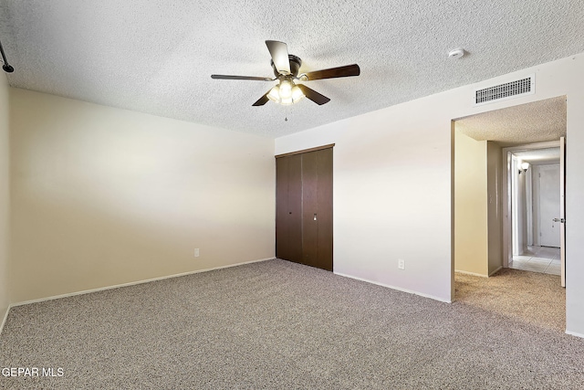 unfurnished bedroom featuring ceiling fan, light colored carpet, a textured ceiling, and a closet