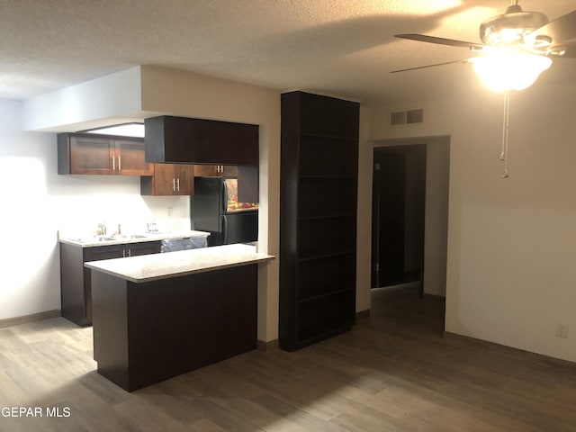 kitchen with dark brown cabinets, black refrigerator, a textured ceiling, ceiling fan, and light wood-type flooring