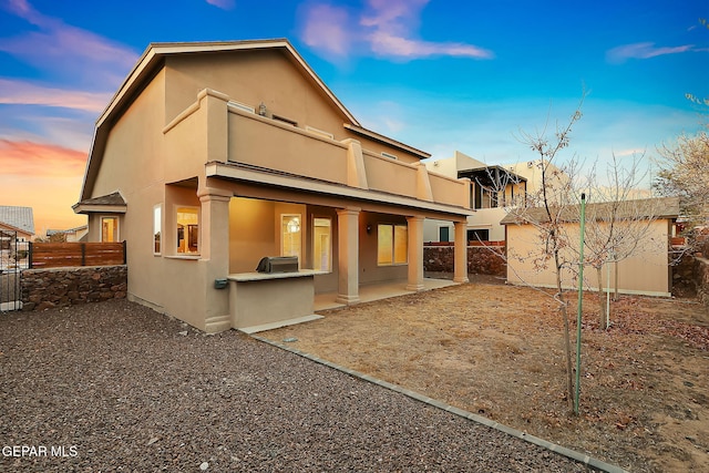 back house at dusk featuring a balcony and a patio