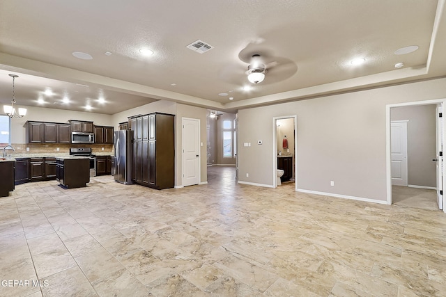 kitchen featuring hanging light fixtures, a raised ceiling, appliances with stainless steel finishes, and dark brown cabinetry