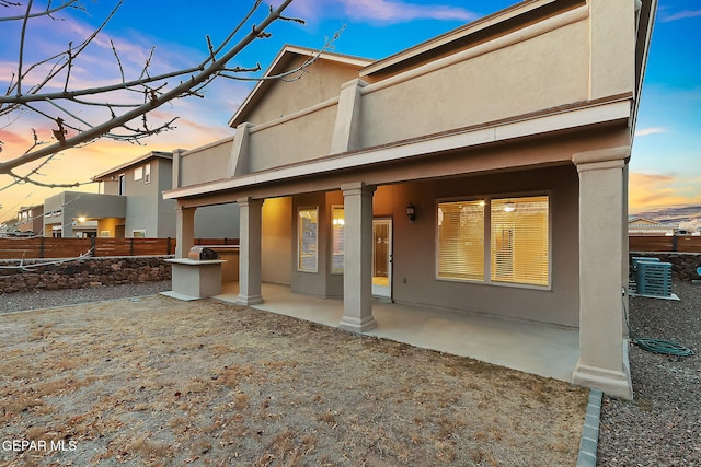 back house at dusk featuring central AC unit and a patio