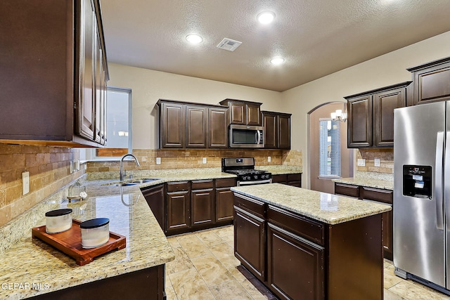 kitchen featuring a kitchen island, appliances with stainless steel finishes, sink, light stone countertops, and dark brown cabinets