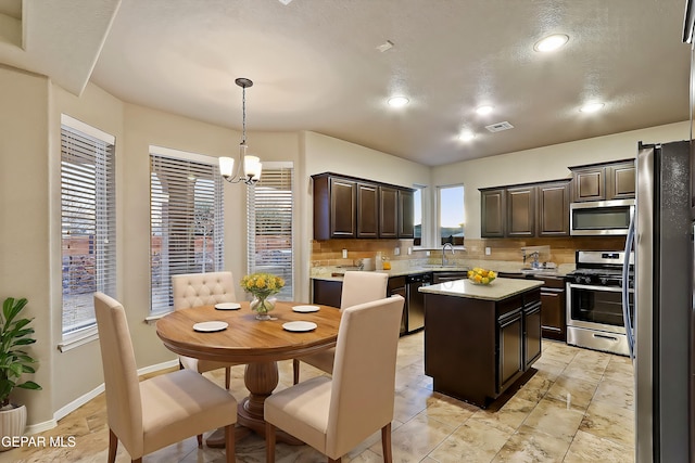 kitchen with sink, stainless steel appliances, dark brown cabinetry, a kitchen island, and decorative light fixtures