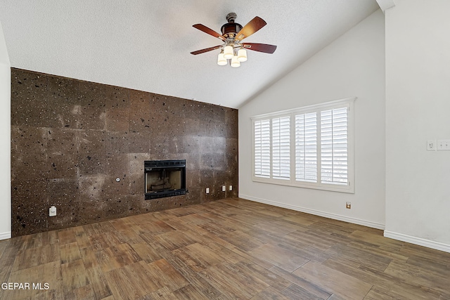 unfurnished living room featuring lofted ceiling, hardwood / wood-style flooring, ceiling fan, a textured ceiling, and a tiled fireplace