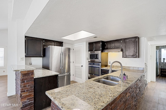 kitchen featuring sink, hardwood / wood-style flooring, stainless steel appliances, a textured ceiling, and kitchen peninsula