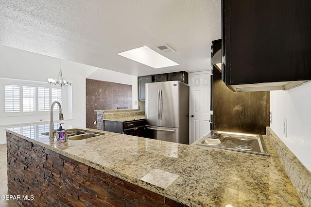 kitchen featuring sink, gas stovetop, a textured ceiling, stainless steel refrigerator, and kitchen peninsula