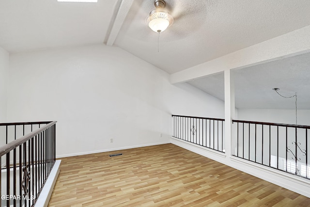 bonus room featuring vaulted ceiling with beams, a textured ceiling, and light wood-type flooring