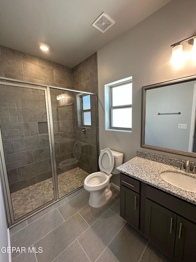 bathroom featuring tile patterned floors, vanity, toilet, and a shower with shower door