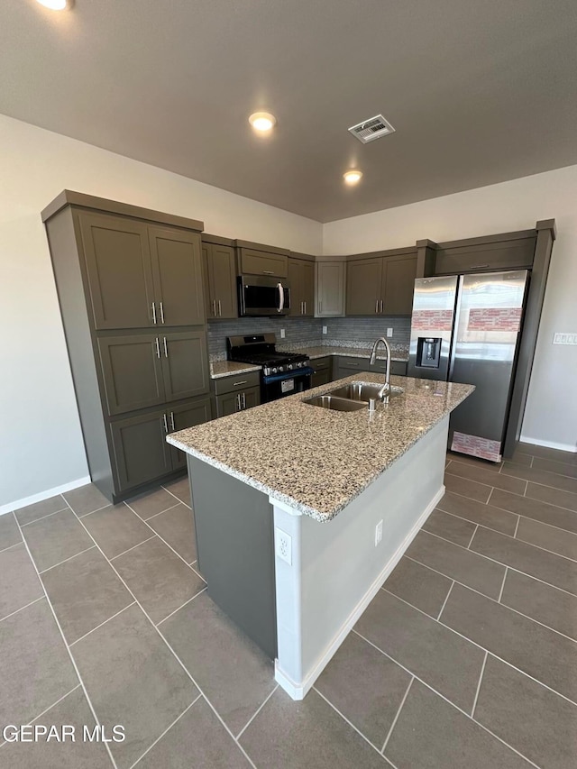 kitchen featuring an island with sink, sink, dark tile patterned floors, stainless steel appliances, and light stone countertops