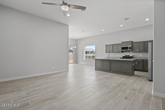 kitchen with pendant lighting, an island with sink, ceiling fan, stainless steel appliances, and light wood-type flooring