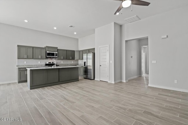 kitchen featuring sink, light hardwood / wood-style flooring, appliances with stainless steel finishes, gray cabinetry, and a kitchen island with sink