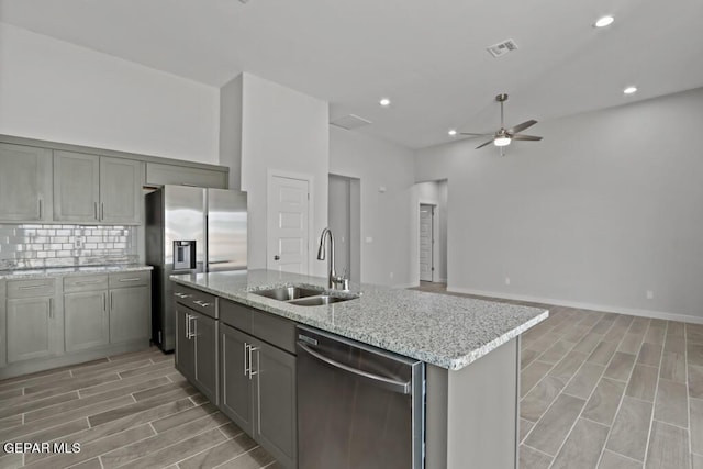 kitchen with an island with sink, sink, backsplash, stainless steel appliances, and light stone countertops