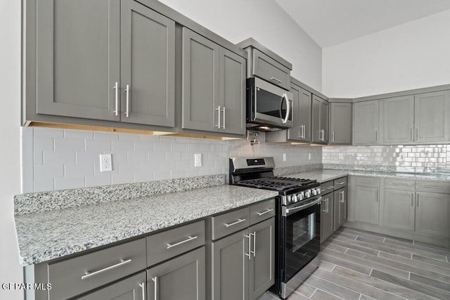 kitchen featuring appliances with stainless steel finishes, gray cabinetry, backsplash, and light stone counters