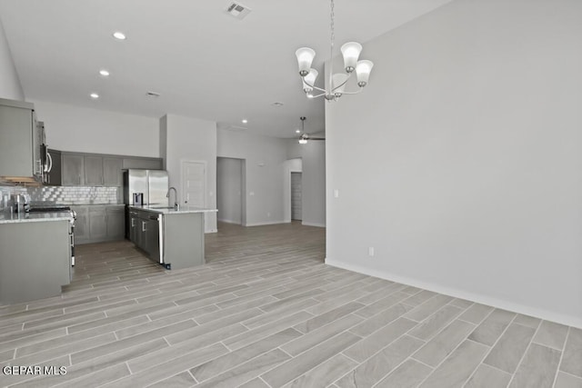 kitchen featuring gray cabinets, a kitchen island with sink, stainless steel appliances, tasteful backsplash, and decorative light fixtures