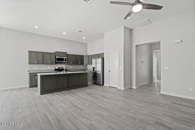 kitchen with sink, a kitchen island with sink, ceiling fan, stainless steel appliances, and light wood-type flooring