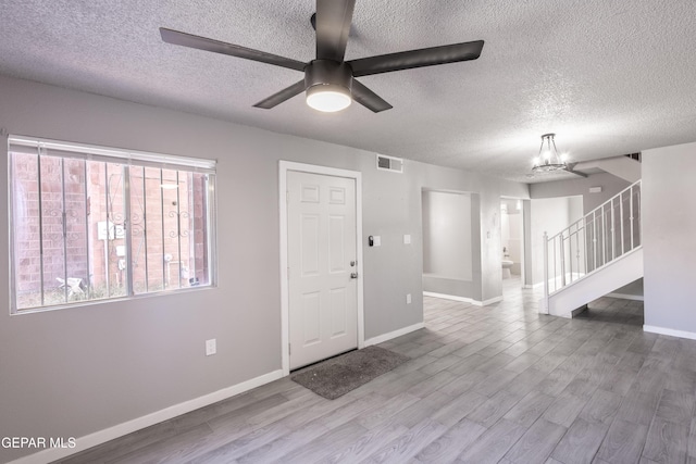 foyer entrance featuring ceiling fan with notable chandelier, light hardwood / wood-style floors, and a textured ceiling