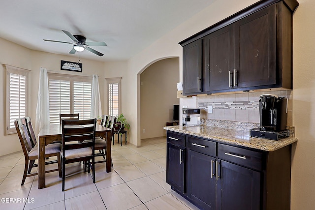 kitchen featuring light stone counters, tasteful backsplash, dark brown cabinets, light tile patterned floors, and ceiling fan