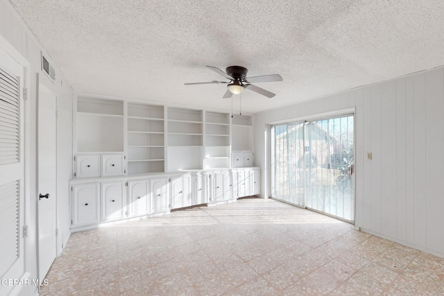 unfurnished living room with a textured ceiling, wooden walls, and ceiling fan