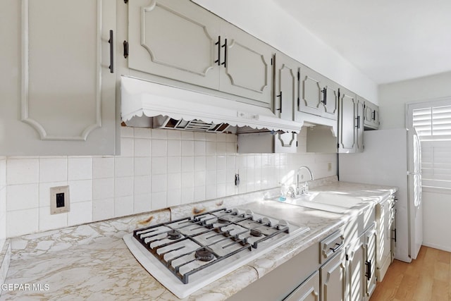 kitchen with sink, white appliances, light hardwood / wood-style flooring, gray cabinets, and backsplash