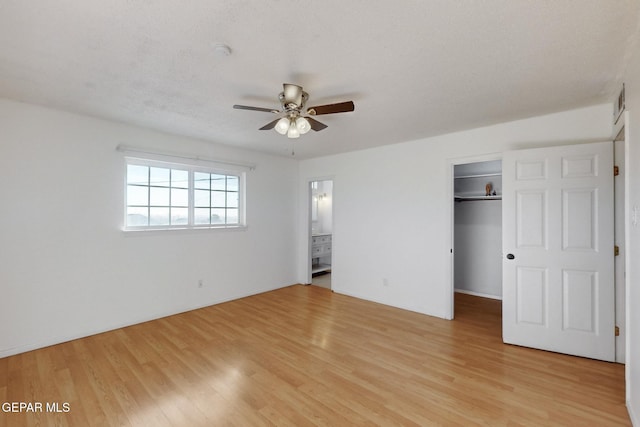 unfurnished bedroom featuring ceiling fan, connected bathroom, light hardwood / wood-style floors, a spacious closet, and a closet