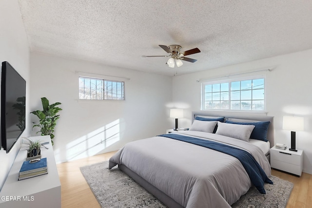 bedroom with multiple windows, a textured ceiling, ceiling fan, and light wood-type flooring