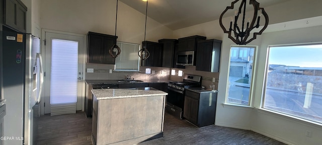 kitchen with appliances with stainless steel finishes, sink, hanging light fixtures, a center island, and light stone countertops