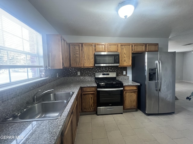 kitchen with sink, backsplash, light tile patterned floors, stainless steel appliances, and a textured ceiling