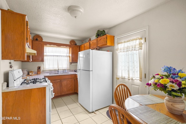 kitchen with sink, white appliances, a textured ceiling, and light tile patterned flooring