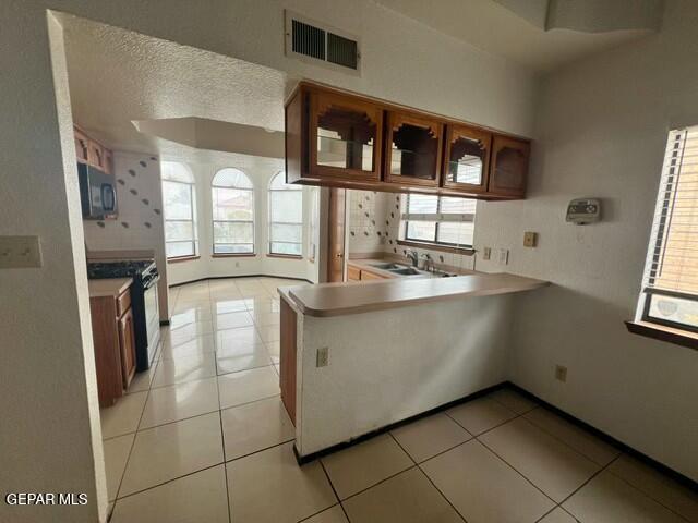 kitchen with light tile patterned flooring, a healthy amount of sunlight, kitchen peninsula, and black appliances