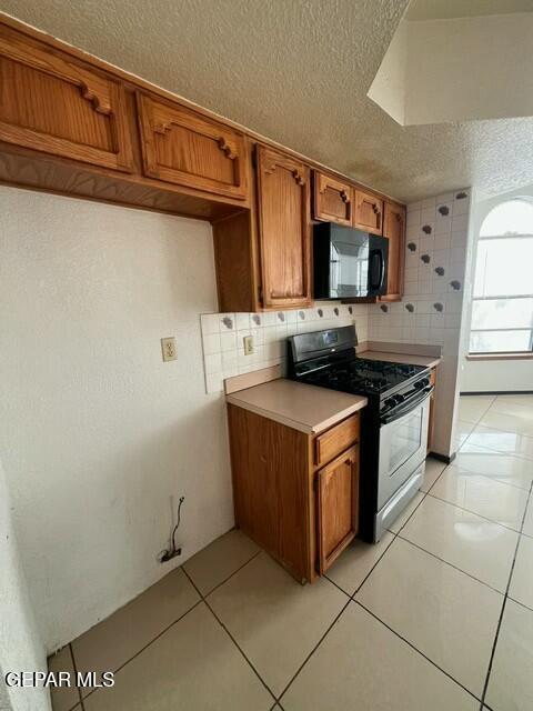 kitchen featuring tasteful backsplash, light tile patterned floors, black appliances, and a textured ceiling