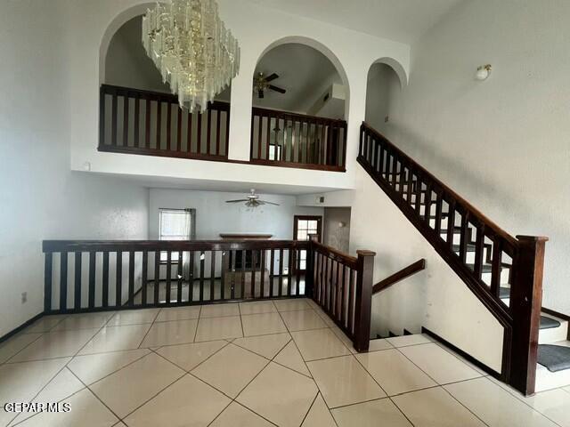 stairs featuring a high ceiling, ceiling fan with notable chandelier, and tile patterned floors